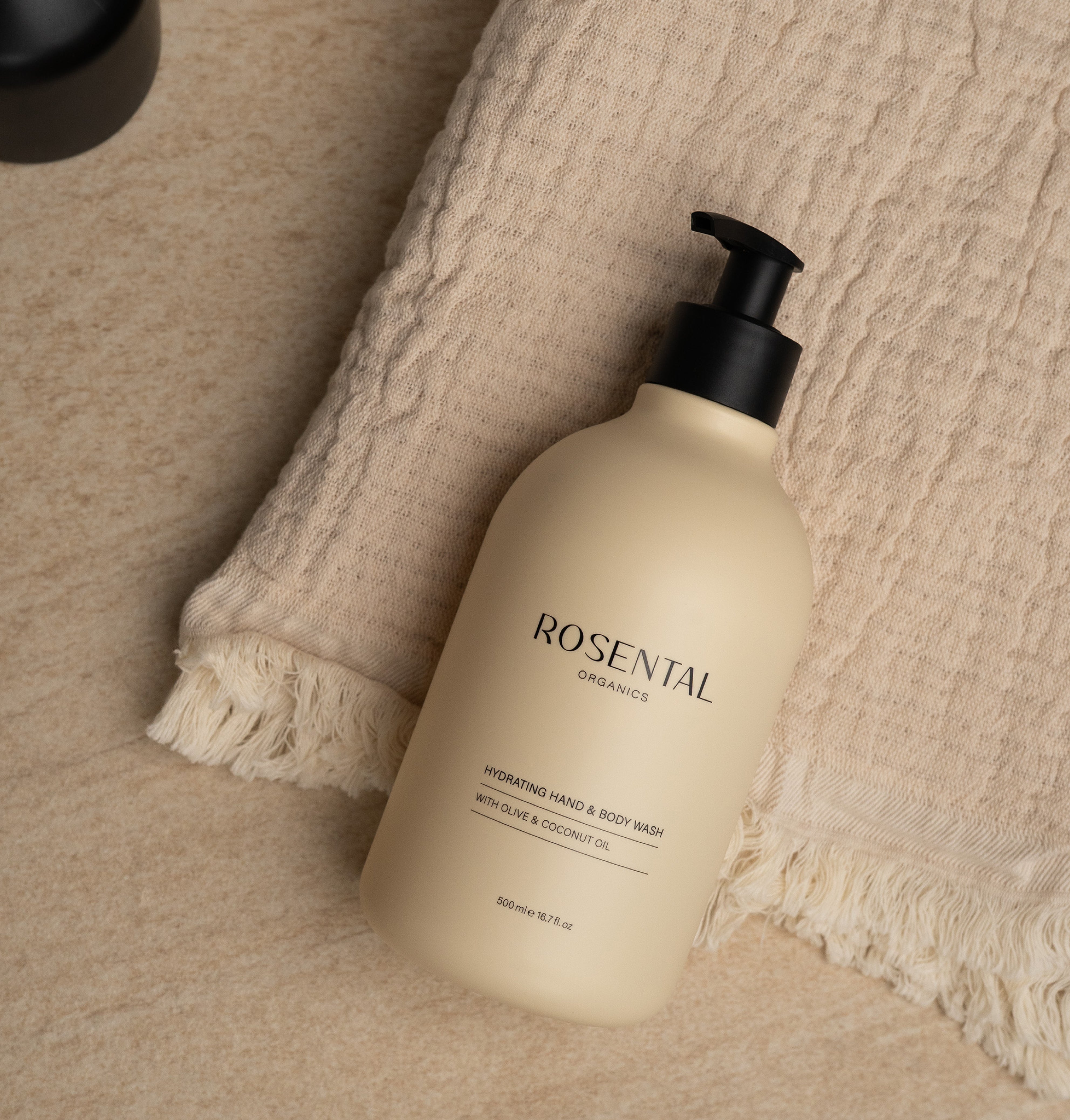 Hydrating Hand & Body Wash in beigefarbenem Pumpspender, liegend auf einem beigen Handtuch auf Marmoroberfläche.