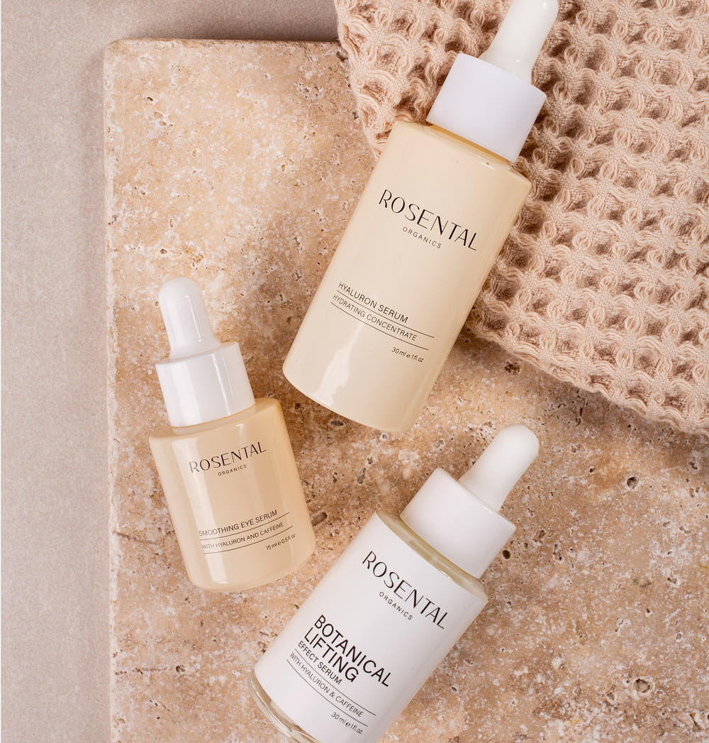 Botanical Lifting Day Routine Produkte von Rosental Organics liegen auf beigefarbenen Marmorstein.