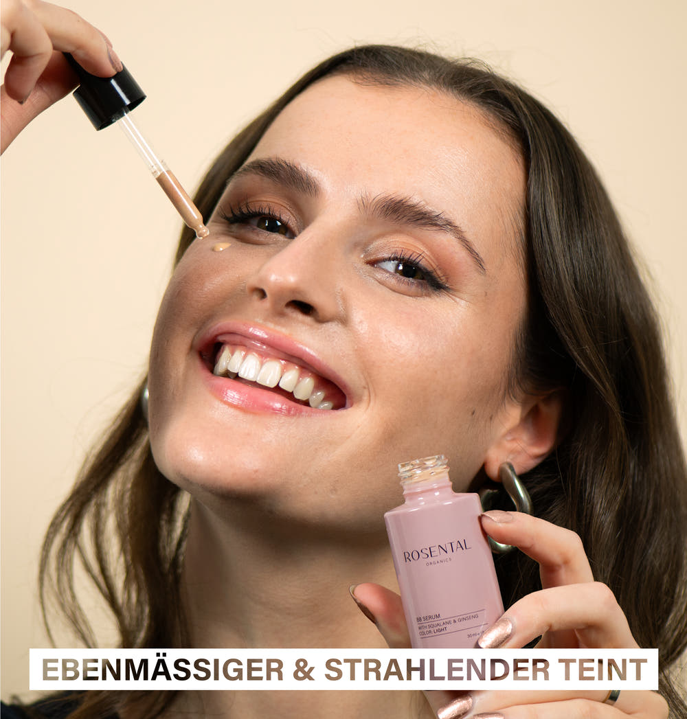 Eine lächelnde Frau trägt das Skin Perfecting Set von Rosental Organics für ein ebenmäßiges Hautbild auf.